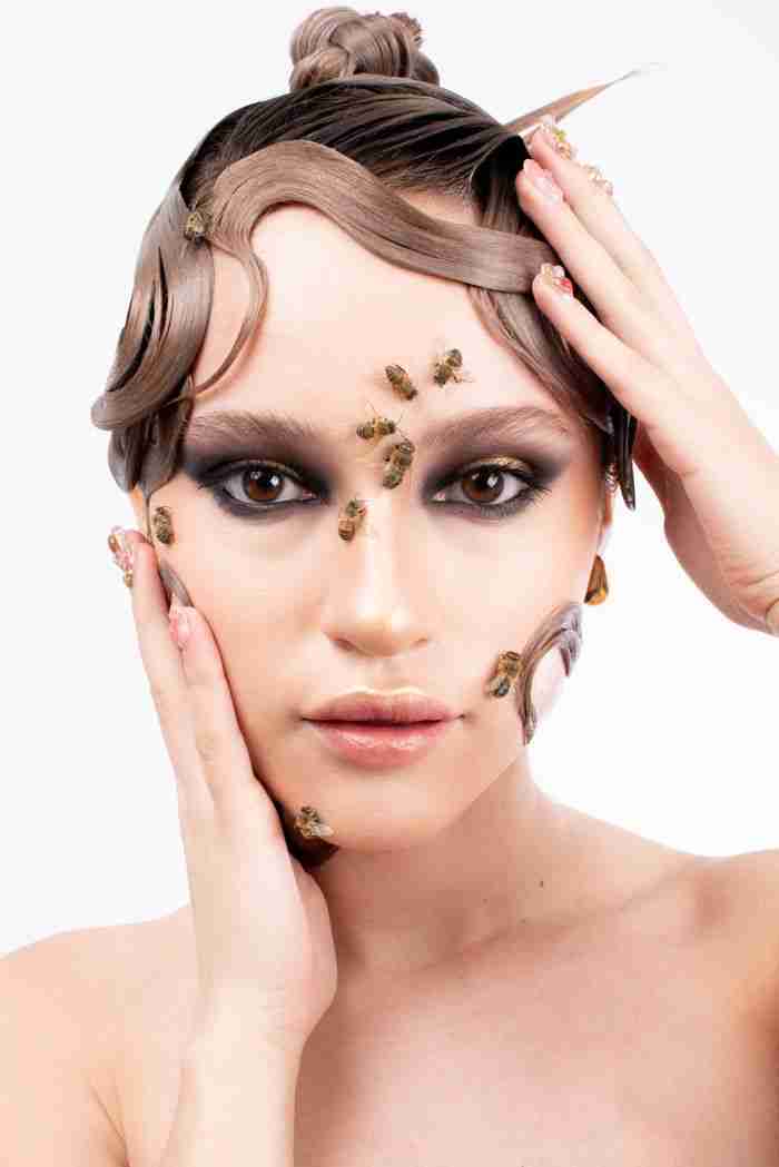 Creative makeup portrait featuring a woman with bees and unique hair styling on a white background.